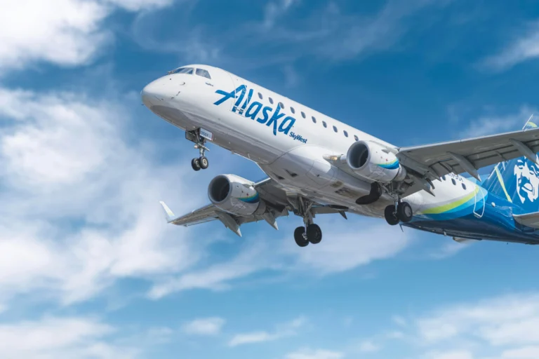 Alaska Airlines passenger plane in flight against a blue sky with clouds.