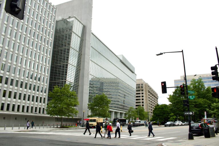 People crossing a street near modern glass office buildings.