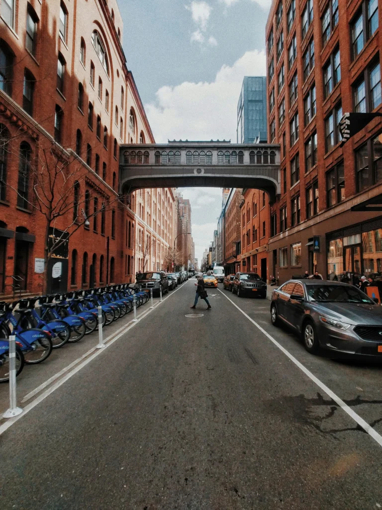 Street view with brick buildings, a pedestrian bridge, and a person crossing the road.