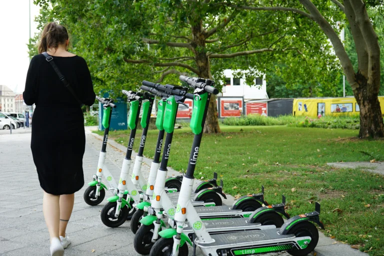 Woman walking past a row of parked Lime electric scooters on a sidewalk.